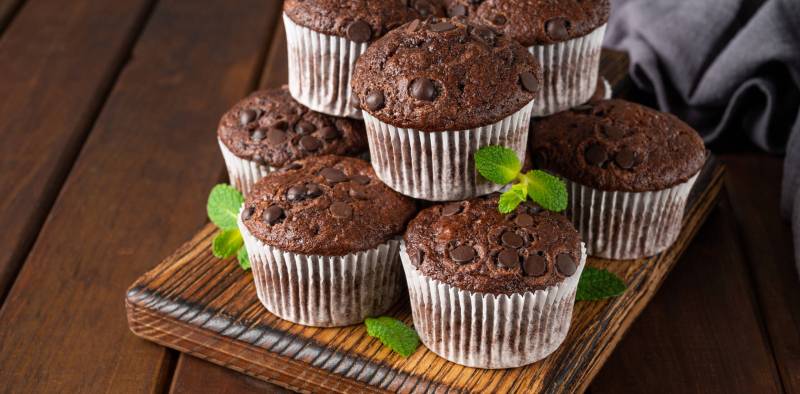Chocolate muffins or cupcakes with chocolate drops on a dark wooden background with fresh berries and mint. Copy space